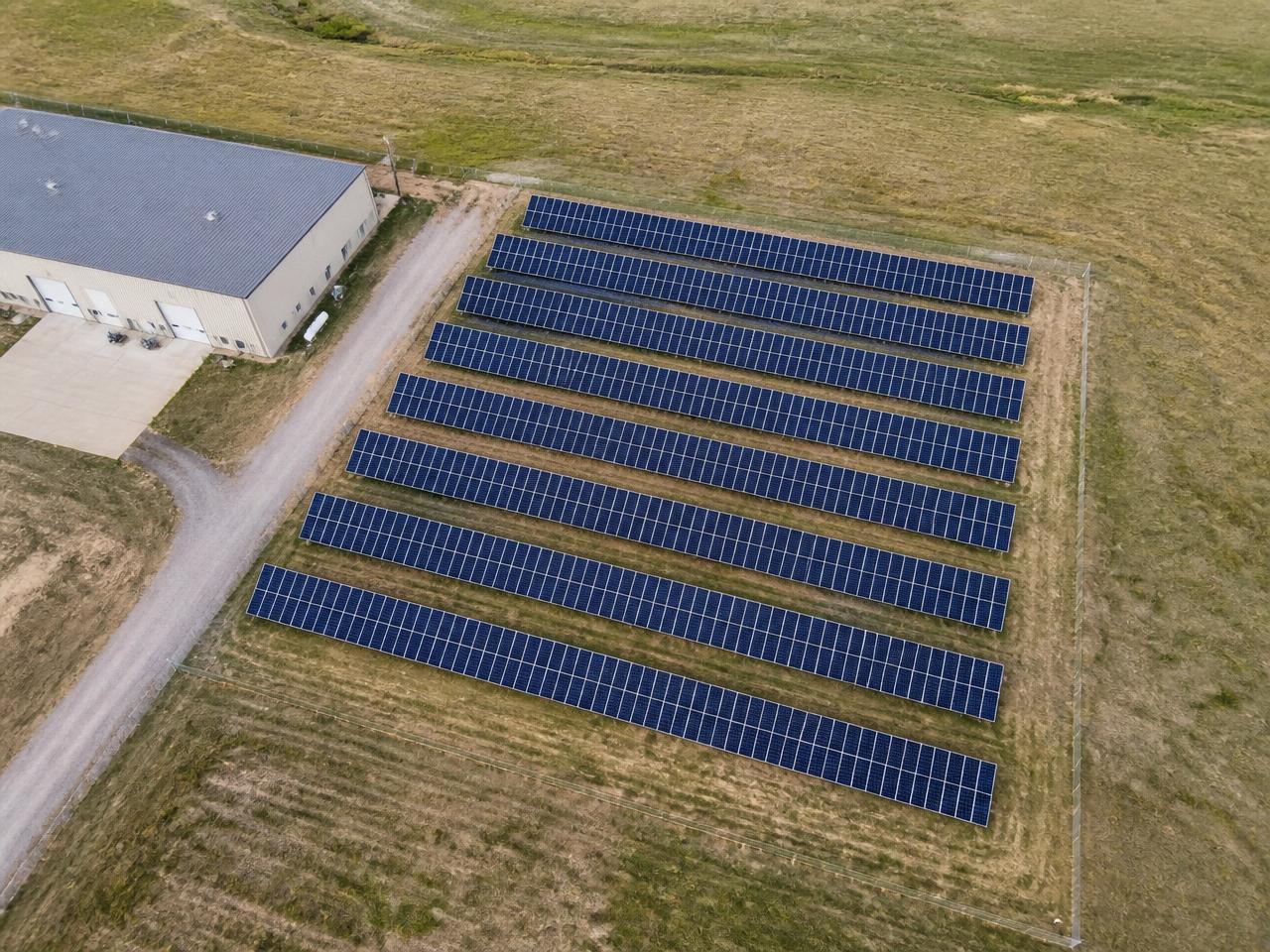 Top-down aerial view of a ground-mounted solar panel array beside a commercial building